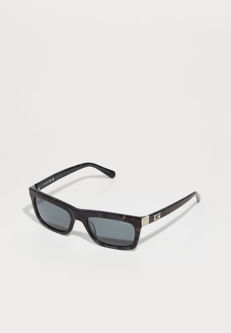 Sorte skilpadde solbriller med rektangulære linser, sølvfarge detaljer og et logo på stangen. Linser i mørkegrå.