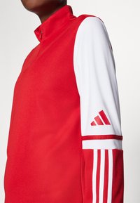 Rød langærmet pullover med høj krave, der har hvide ærmer og røde striber. Indeholder Adidas-logo i rødt på venstre arm. Glat tekstur.