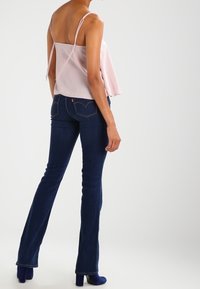 Top suelto color rosa claro con tirantes finos; combinado con jeans acampanados de color azul oscuro, que cuentan con un diseño clásico de cinco bolsillos.