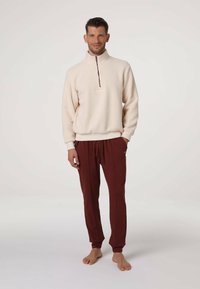 Pullover in pile color crema con mezza zip e polsini a coste, abbinato a pantaloni della tuta color bordeaux con vita elasticizzata e tasche laterali.