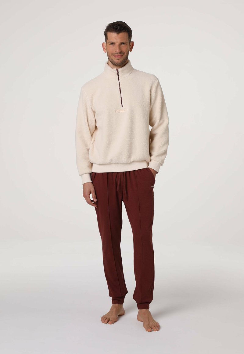Pullover in pile color crema con mezza zip e polsini a coste, abbinato a pantaloni della tuta color bordeaux con vita elasticizzata e tasche laterali.