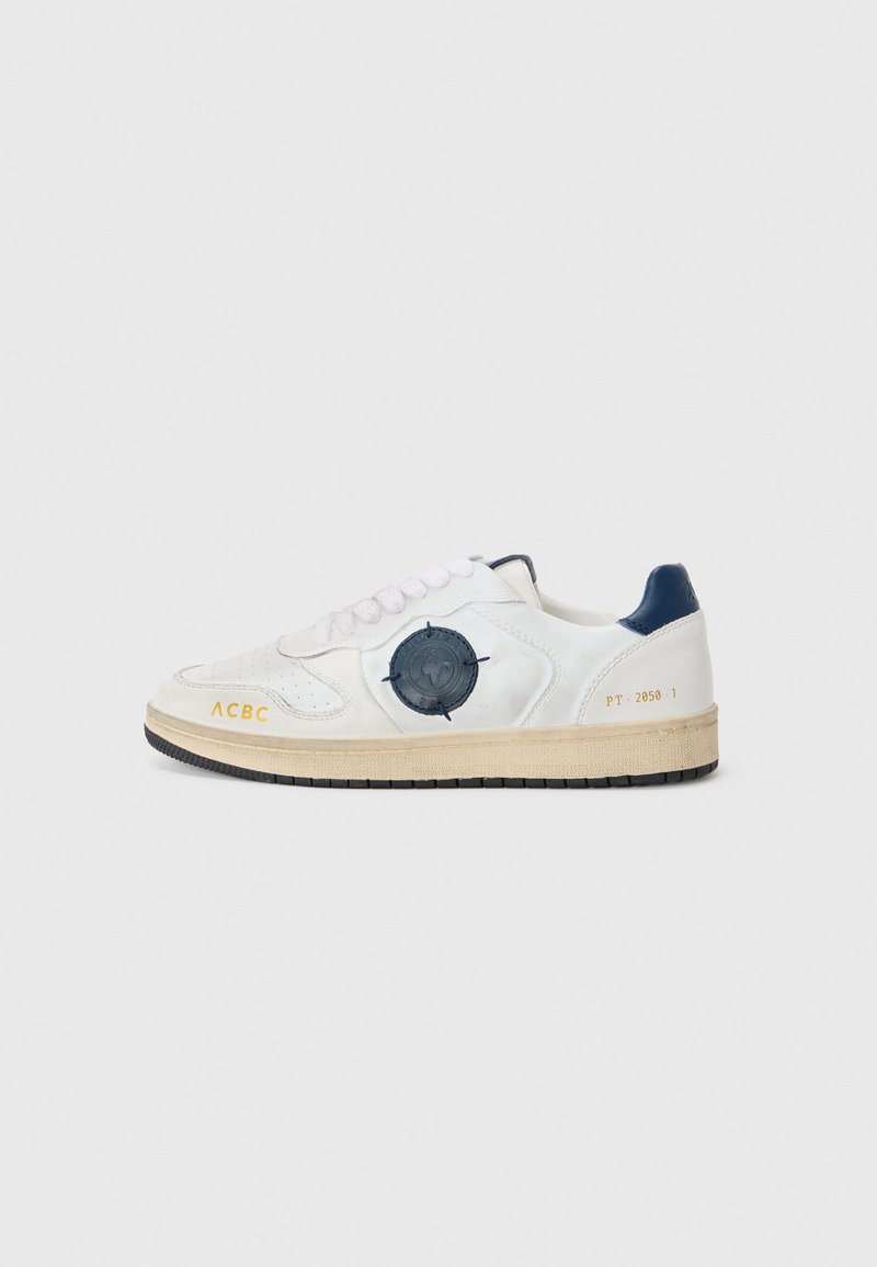 Hvite skinn sneakers med en teksturert blå aksent på siden, rund emblem og svart gummisåle. Inkluderer snøringer og merkevaredetaljer.