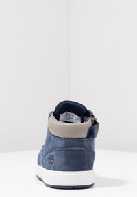 Tmavě modré semišové vysoké tenisky s světle šedým límcem kolem kotníku, bílou mezipodešví a detailem loga na patě. Viditelný zip.