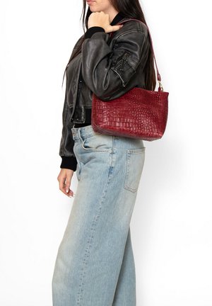 Sac à main en simili cuir bourgogne avec un motif crocodile texturé, poignée courte et ouverture en haut, porté sur une épaule sur fond blanc.