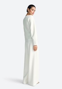 Valge pikka varrukatega top, mida kannab laia säärega püksid, mõlemad valmistatud sileda kangaga. Topil on ümar kaelus ja peened õmblused.