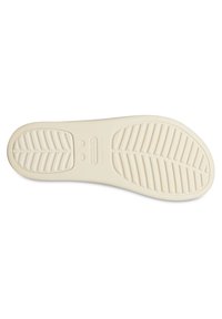 Suola di Crocs, colore beige chiaro, materiale in gomma, presenta un motivo testurizzato con scanalature per una presa migliore e due indentazioni circolari.