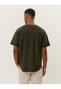 T-shirt corto a maniche corte di colore verde scuro con collo rotondo e taglio rilassato. La vista posteriore mostra un orlo dritto e un tessuto morbido e testurizzato.