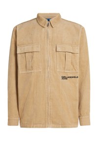 Beige korkkangast sahvrätik, millel on kokku tõmmatav esi, krae, kaks rinna-taskut ning musta värvi brodeeritud "KARL LAGERFELD JEANS" logo. Tekstureeritud kangas.