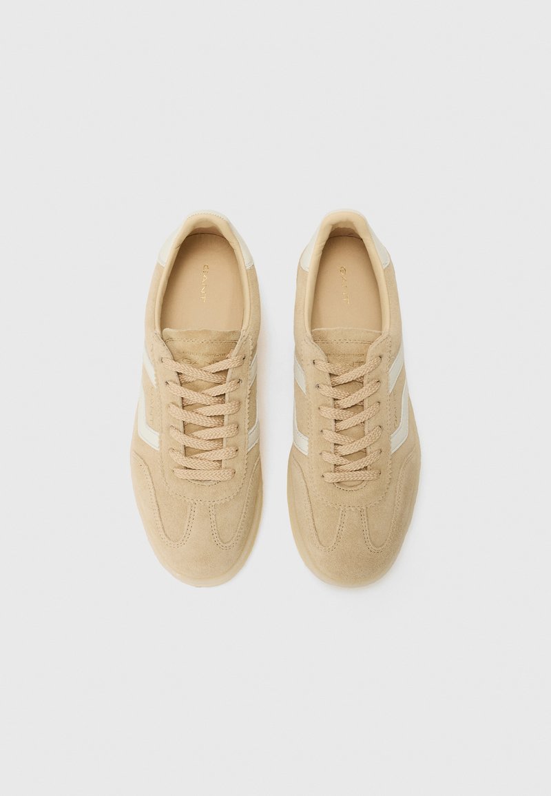 Beige Wildlederschuhe mit weißen Seitenschienen, runder Spitze, Schnürverschluss, strukturiertem Obermaterial und Branding auf der Zunge.