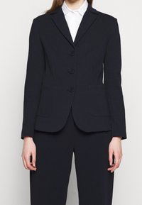 Blazer de navy con un diseño estructurado, de un solo botón, con tres botones en el frente, solapas con muescas y dos bolsillos frontales. Textura suave.