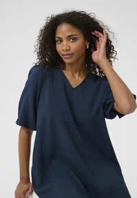 Navy blue, short-sleeve dress with a V-neck and textured fabric. Loose fit with subtle crinkle detail, offering a relaxed silhouette.