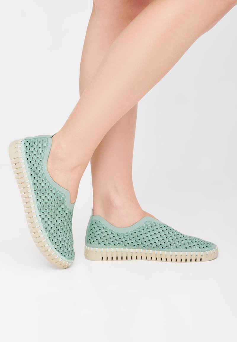 Scarpe slip-on verde menta con design perforato, tomaia flessibile e suola texturizzata di colore crema con scanalature per la presa.