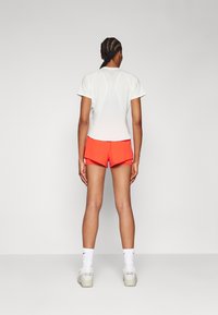 Camiseta atlética blanca de manga corta y pantalones cortos rojos brillantes. La camiseta tiene un escote redondo y detalles en la parte posterior; los pantalones cortos tienen aberturas laterales.
