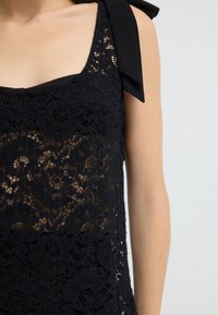 Sort blonde top med firkantet udskæring og stofsløjfe på skulderen. Blonderne har et blomstermønster med en let gennemsigtig tekstur.