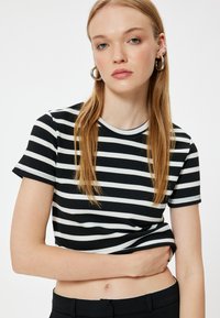 Top de rayas blanco y negro de manga corta con textura acanalada y escote redondo, que presenta un diseño ajustado y una longitud corta.