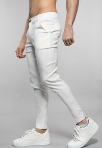 Pantalon blanc skinny en tissu léger, avec une fermeture à bouton, des poches latérales et des jambes fuselées. Assorti avec des baskets blanches.