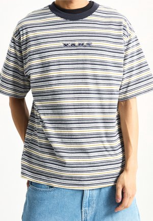 Person wearing a striped Vans t-shirt with black, white, and yellow lines, paired with light blue denim jeans.