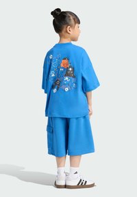 Modrý bavlnený sveter a šortky s farebnou grafikou rôznych kreslených postavičiek na zadnej strane.