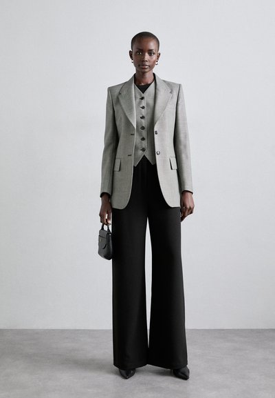 Harmaa, ruutukuviollinen bleiseri, jossa on vastaava liivi, yhdistettynä leveälahkeisiin mustiin housuihin ja teräväkärkisiin mustiin korkokenkiin. Pieni musta käsilaukku, yksinkertaiset korvakorut.