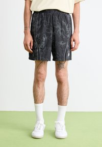 Pantaloncini sportivi neri con un motivo grigio a spirale, vita elasticizzata e due tasche laterali. Indossati con sneakers bianche e calzini.
