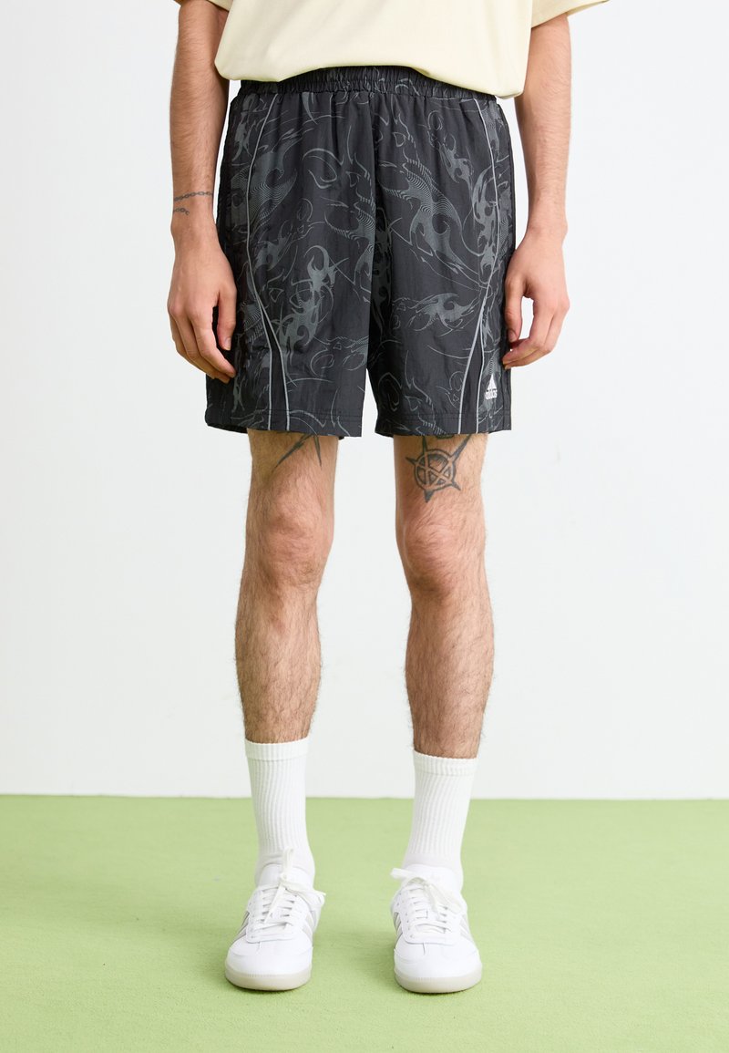 Pantaloncini sportivi neri con un motivo grigio a spirale, vita elasticizzata e due tasche laterali. Indossati con sneakers bianche e calzini.
