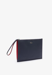 Pochette bracelet bleu foncé avec intérieur rouge et fermeture éclair argentée, avec un petit logo crocodile argenté sur le devant.