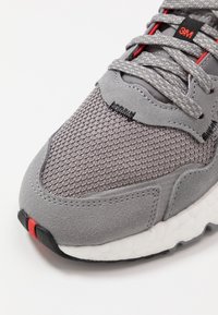 Šedé tenisky s materiály z meshu a suède, texturovaný svršek se šedými tkaničkami, červenými akcenty a bílou tlumící mezipodešví.