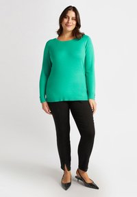 Turkusowy sweter dzianinowy z okrągłym dekoltem, czarne dopasowane spodnie oraz czarne szpilki z wydłużonym noskiem, zdobione ćwiekami.