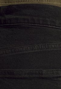 Tela de mezclilla negra con una cinturilla acanalada de color verde oliva. Presenta líneas de costura horizontales y una textura suave.