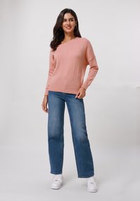 Sweater tricoté rose clair avec une coupe ample et une encolure large, associé à un jean en denim bleu taille haute et des baskets blanches.