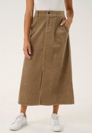 Vrouw draagt een knielange beige corduroy rok met een split aan de voorkant en zakken, gecombineerd met witte sneakers en een ingestopt wit topje.