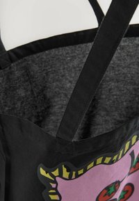 Black apron with black straps, featuring a large pink graphic with red tomatoes and yellow stripes on the top edge, made of textured fabric.