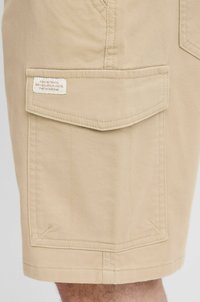 Kaki shorts laget av teksturert bomullsblanding. Har sidelomme med klaff og sømdetaljer. Merket er sydd på lommen.