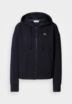 Tumesinine tõmblukkudega kapuutsiga pluus, mis on valmistatud pehmest puuvillakangast. Omab esist pocketit, reguleeritavat kapuutsi, soonikkoes varrukaid ja väikest tikandit.