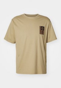 Beige katoenen t-shirt, ronde hals, korte mouwen. Heeft een zwart Timberland logo op de linkerborst. Glad textuur.