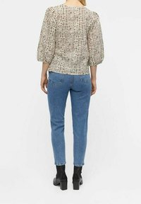 Haut beige clair avec un motif à carreaux, manches bouffantes ; associé à un jean bleu et des bottines noires ; tissu lisse, coupe décontractée.