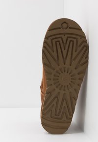 Cizmă din suede maro cu o talpă din cauciuc texturat. Talpa are un model în explozie de stea cu brandul, în unghi, pe un fundal alb.
