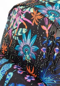 Mochila floral con una tela negra adornada con flores coloridas, enredaderas y hojas, con detalles de cremallera y cuerdas negras.