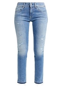 Jeans de denim azul claro con un corte ajustado, que presentan detalles desgastados y dobladillos deshilachados. Diseño estándar de cinco bolsillos con cierre de botón.