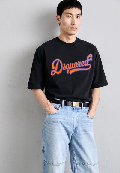 Tricou negru cu logo-ul "Dsquared²" în roșu și albastru, asociat cu blugi de denim oversized, de culoare bleu deschis, și o centură neagră cu detalii aurii.