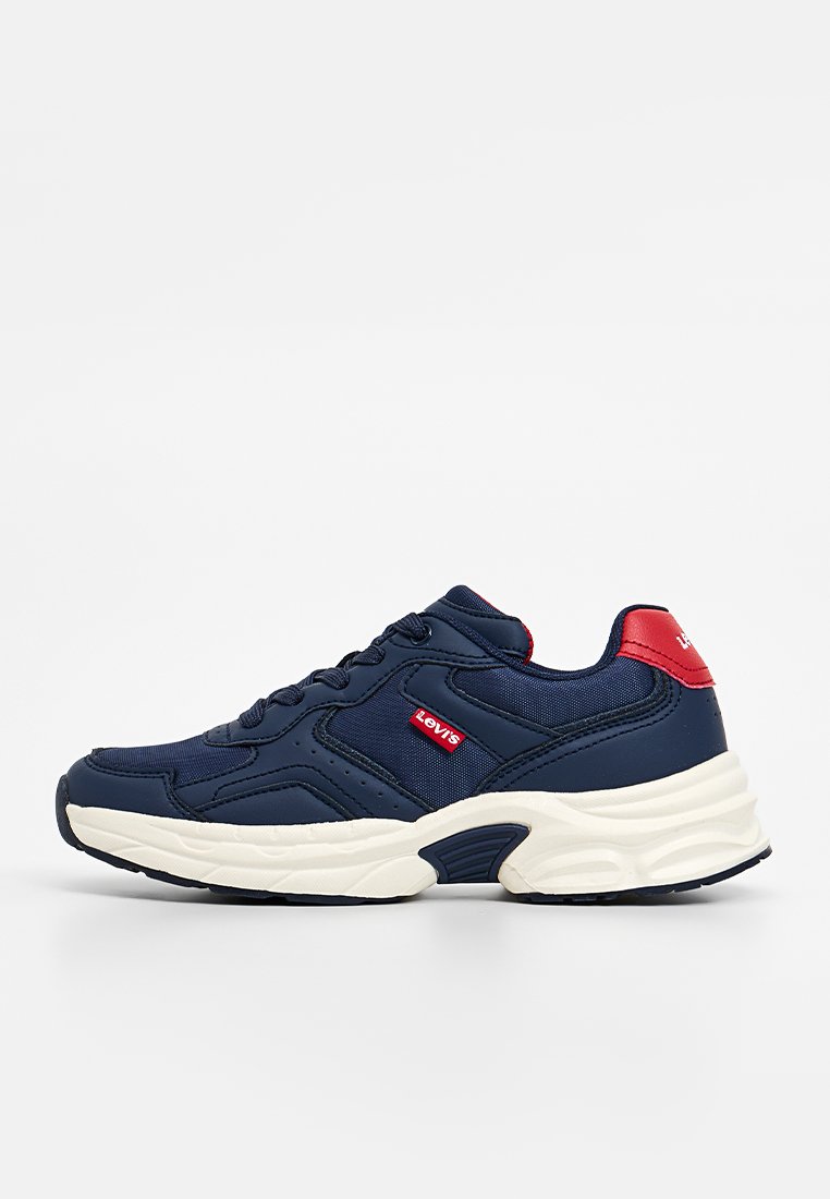 Zapatilla deportiva azul marino con tejido texturizado, media suela blanca, acentos rojos y diseño de cordones que incluye un logo en el costado.