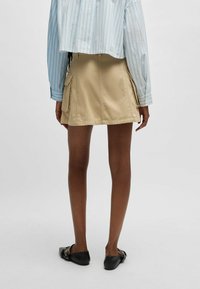 Beige cargo mini-nederdel med sidelommer, lavet af letvægtsstof, med lige snit og glat tekstur. Sorte slip-on-sko.