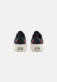 Sneakers neri in tela con suole in gomma bianca, ciliegie rosse ricamate sul tallone e branding "CONVERSE ALL STAR" sul retro.