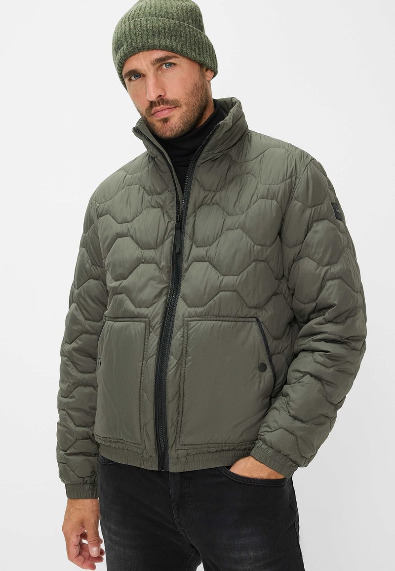 Polstret jakke i olivengrøn med quiltet design, frontlynlås og to store lommer. Har en stående krave og elastiske manchetter.