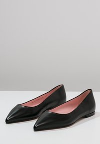 Bailarinas de piel negra con un diseño de punta afilada y un interior rosa. Textura suave con una suela de perfil bajo, adecuadas para uso casual o formal.