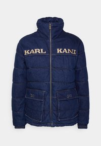 Marinblå denimpuffjacka med hög krage, dragkedja och två framfickor. Guld broderad "KARL" och "KANI" på bröstet. Sticksömn detaljer.