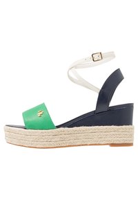 Grön och marinblå kilklack sandal med en vit ankelrem, har en vävd jute-såle och en liten gulddetalj på den gröna delen.