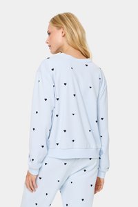Sudadera azul claro con estampados de corazones negros, corte relajado, cuello redondo y puños de canalé. Combinada con pantalones a juego para un look coordinado.
