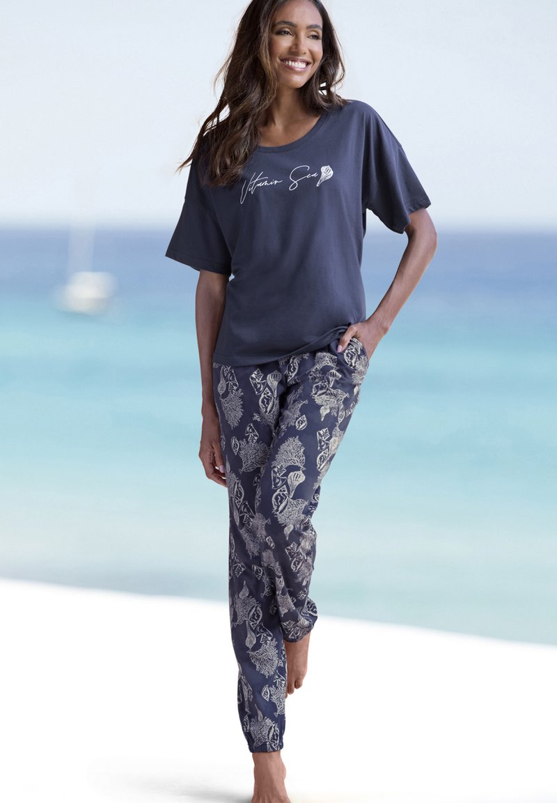 Marineblaues T-Shirt mit dem Text "Vitamin Sea"; blumenmusterte, leichte Hose in Blau- und Beigetönen; lässige Passform und weiche Textur.