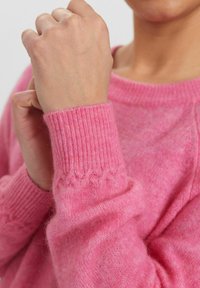 Rožinė megzta palaidinė su raukšlėmis ant rankovių, turinti tekstūrinį raštą ant rankovės. Minkšta, lengva medžiaga su šiek tiek pūkuotu paviršiumi.